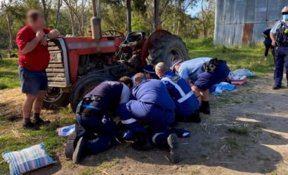 Patient is being assessed by clinical staff, near the tractor from which he fell